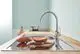 Grohe Einhand-Spültischbatterie mit hohem Auslauf in chrom, montiert an einer Holzarbeitsplatte, neben einer Schale mit Süßkartoffeln und einem Topf im Hintergrund.