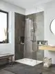 Dusche mit moderner Grohe Kopfbrause, fließendem Wasserstrahl, transparentem Duschabtrennung, grauen Fliesen und Holzregal in hellem Bad.