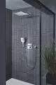 Dusche mit modernen, grauen Wandfliesen und einer Grohe Handbrause. Die Wand ist in schmalen vertikalen Streifen gestaltet. Im Hintergrund befindet sich ein Pflanzelement in einem Topf.