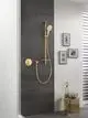 Grohe Handbrause mit goldener Oberfläche, an einer Wand aus dunklen Fliesen montiert. Dazu ist ein Duschthermostat und eine Ablagefläche sichtbar.