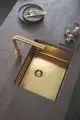 GROHE Spüle mit goldfarbenem Finish und integrierter Armatur, auf einer Arbeitsplatte aus grauem Material, neben einem Teller und Pilzen auf einem Holzbrett.