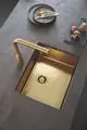 Grohe Spültischarmatur in goldfarbenem Finish mit herausziehbarem Schlauch und dazu passendem Spülbecken in der gleichen Farbe, platziert auf einer grauen Arbeitsfläche.