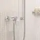 GROHE Brausebatterie in Chrom-Optik, wandmontiert, mit einer Handbrause und schlauch, an einer gefliesten Wand mit hellen Kacheln und Ablagefläche für Pflegeprodukte.