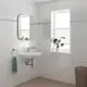 Weißes Waschbecken mit verchromtem Wasserhahn und einem runden Spiegel über der Wandmontage. Pflanze am Fenster und Handtuchhalter mit Handtuch. Grohe-Produkte sind deutlich sichtbar.