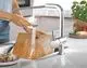 Küchenarmatur von Grohe mit ausziehbarer Spülbrause, die Wasser auf ein Schneidebrett leitet. Im Hintergrund sind frische Kräuter und ein Teller sichtbar.