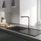 Grohe Armatur mit einem hohen, flexiblen Auslauf und einer separaten Spülbrause, platziert auf einer dunklen Küchenarbeitsplatte neben Brot auf einem Holzbrett.