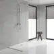 Duschsystem von Grohe mit Handbrause und Einhandmischer in chrom, montiert an einer hellen Wand. Neben der Duschfläche steht ein Holzstuhl mit gestapelten Handtüchern.