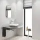 GROHE Waschplatz mit rundem Waschbecken und chromfarbener Armatur. Spiegel an wandmontierter Fläche über grauem Tisch. Fenster mit Jalousie und rumstehendem Beistelltisch.