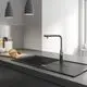 Küchenszene mit einem Grohe Wasserhahn und einem schwarzen Spülbecken. Auf der Arbeitsplatte befinden sich Brot und Küchenutensilien. Helle Wände und moderne Lampe im Hintergrund.
