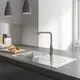 Grohe Küchenarmatur mit einem schlanken, chromfarbenen Auslauf. Neben der Armatur befindet sich ein Spülbecken und eine Holzplatte mit Brotscheiben und Küchenutensilien.