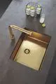GROHE Küchenarmatur in Gold mit integriertem Bedienhebel. Der Sinkbereich ist in dunklem Material mit goldfarbener Spüle und Abfluss gestaltet. Brandsymbol gut sichtbar.