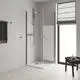 Duschbereich mit klaren Glasschiebetüren, handgehaltenem Duschkopf und Griffstangen. Grohe-Brausebatterie sichtbar montiert an der Wand. Holzfußboden und Fenster mit Sonnenschutz.