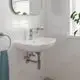 Waschbecken mit Grohe Armatur in einem hellen Badezimmer. Weiße Fliesen an den Wänden, ein Spiegel über dem Becken und eine Pflanze im Fenster. Handtuchhalter an der Seite.