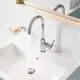 Waschtisch mit verchromter Grohe Armatur, die Wasser aus dem Auslauf strömt. Neben der Armatur ist eine Seifenablage mit einer Seife sichtbar. Weiße Kacheln im Hintergrund.