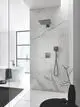 Dusche mit GROHE Handbrause und Regenkopf in hard graphite, montiert an einer marmorierten Wand. Sichtbare Bedienungselemente für die Wassersteuerung.