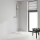 Duschbereich mit verchromter Brausestange von Grohe an einer weißen Wand. Sichtbarer Duschkopf und eine Duschwanne in der Ecke. Helles Holzfußboden und Fenster mit Rollo.