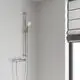 Helle Wand mit einer verchromten Brausestange von Grohe, die einen Handbrausekopf hält. Links im Bild ist ein Fenster mit einem verdunkelnden Rollo zu sehen.