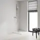 Duschbereich mit Grohe Brausegarnitur, Handbrause und verchromtem Haltegriff. Neben Fenster und schwarzem Beistelltisch mit Pflegeprodukten auf hellem Boden.