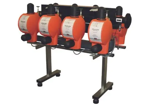 Ein Gerät mit vier orange-farbenen, runden Kammern, die auf einem stabilen Metallgestell montiert sind. Jede Kammer hat eine Beschriftung und Verbindungsschläuche.