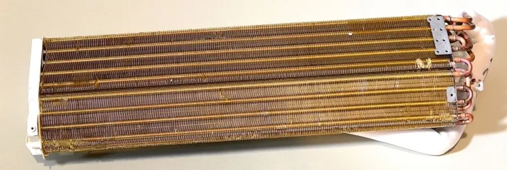 Verdampfer von Remko mit mehreren Kupferrohren und Lamellen. Das Bauteil ist länglich und hat einen weißen Kunststoffabschluss an einem Ende.
