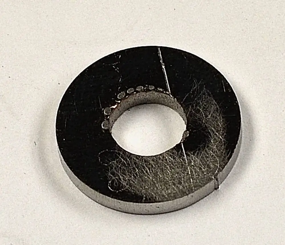 Schwarze, runde Metallplatte mit mittigem Loch und feinen Kratzern sowie Staub, möglicherweise von einem Remko-Produkt.