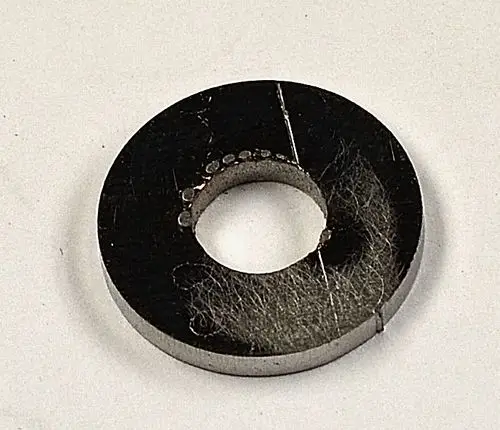 Schwarze, runde Metallplatte mit mittigem Loch und feinen Kratzern sowie Staub, möglicherweise von einem Remko-Produkt.