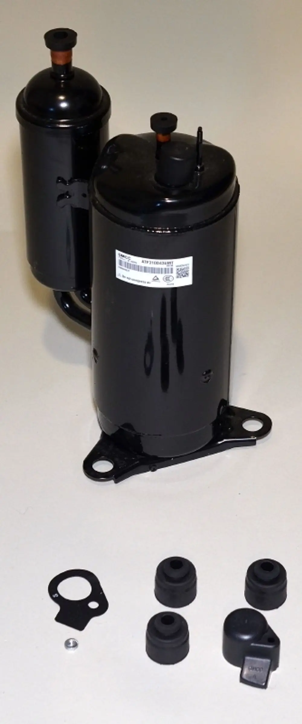 Zwei schwarze Kompressoren von Remko mit Anschlussrohren und verschiedenen Gummiteilen sowie einer Dichtung und Schraube darauf liegend.