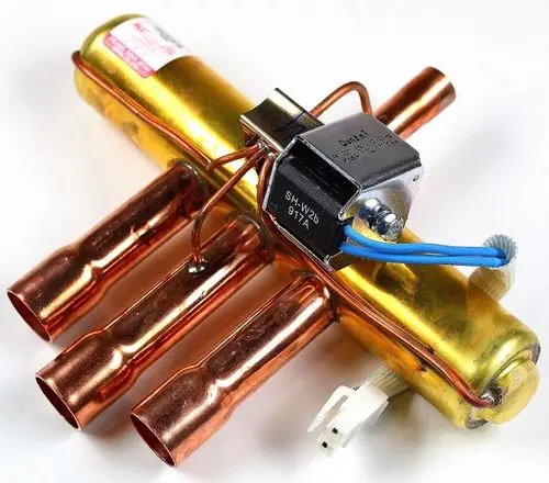 4-Wege-Umkehrventil von Remko mit vier Kupferleitungen und einem elektrischen Anschluss. Es handelt sich um ein technisches Bauteil für Heiz- oder Kühlsysteme.
