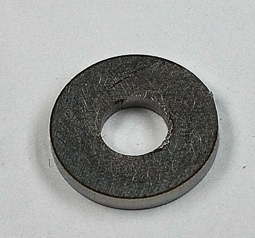 Graue, runde Metallscheibe mit innenliegendem Loch, auf weißem Hintergrund. Möglicherweise Teil eines größeren Systems von Remko.