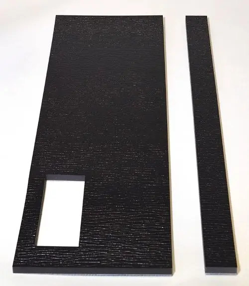 Schwarze Dämmplatten von Remko, eine große Platte mit rechteckigem Ausschnitt und eine schmale lange Platte. Strukturierte Oberfläche, auf hellem Hintergrund.