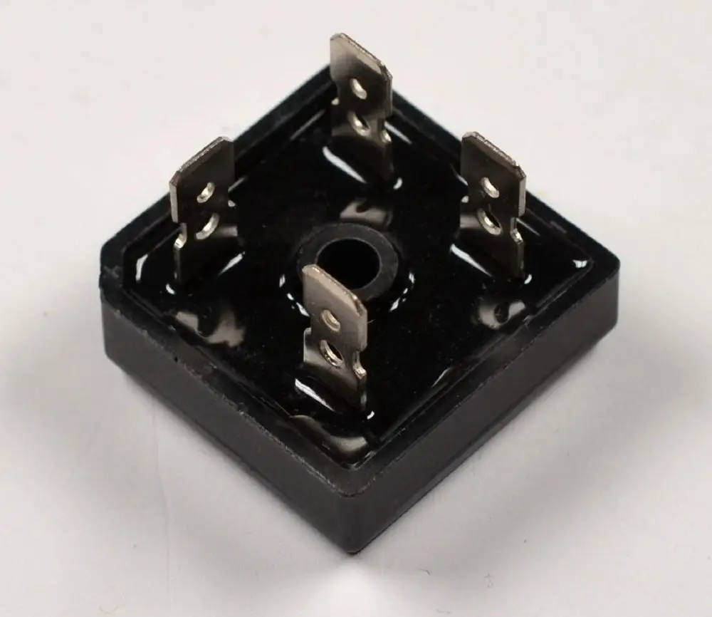 Gleichrichter mit quadratischer Grundform, vier Anschlussklemmen und einer zentralen Bohrung. Produkt von Remko, geeignet für DC-Anwendungen.