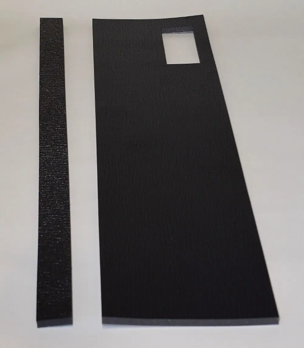 Schwarze Dämmplatten von Remko, eine größere rechteckige Platte mit einem rechteckigen Ausschnitt und eine schmale Leiste, auf einem neutralen Hintergrund.