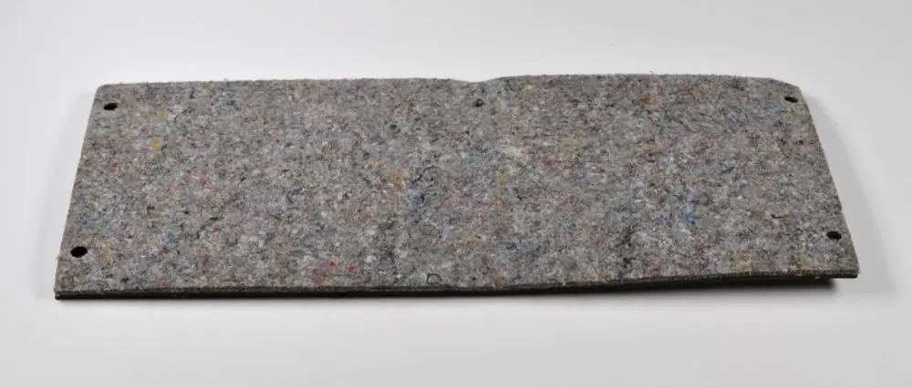 Seitliche Abdeckung aus strukturiertem Material, eventuell von Remko, mit zwei Befestigungslöchern an den Seiten. Farbspektrum in Grau mit bunten Einschlüssen sichtbar.