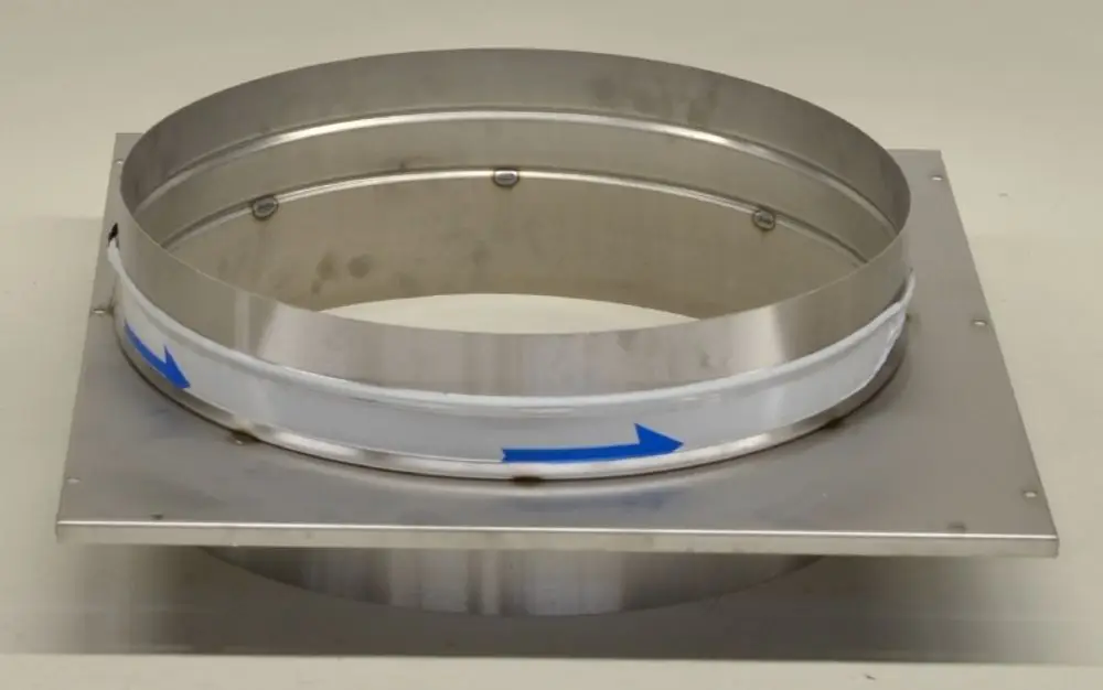 Metallischer Auslass mit runder Öffnung, montiert auf einer rechteckigen Grundplatte. An der Außenseite sind Pfeile zur Richtungsanzeige angebracht. Produkt von Remko.