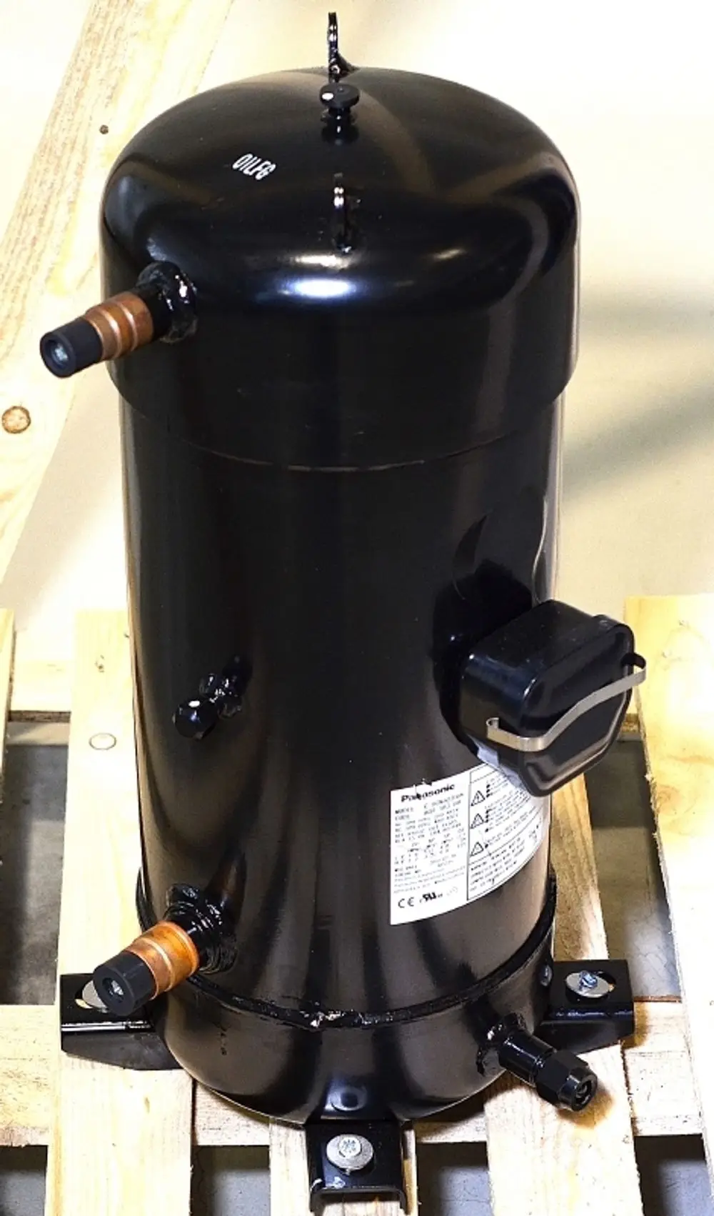 Schwarzer Kompressor von Remko mit zwei Kupferrohren und einer elektrischen Anschlussvorrichtung, montiert auf einer Holzpalette.