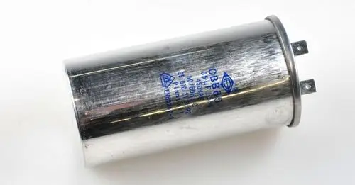 Kondensator für Kompressor, metallische Oberfläche mit Anschlussstiften, beschriftet mit technischen Angaben. Produkt von Remko für elektrische Anwendungen.
