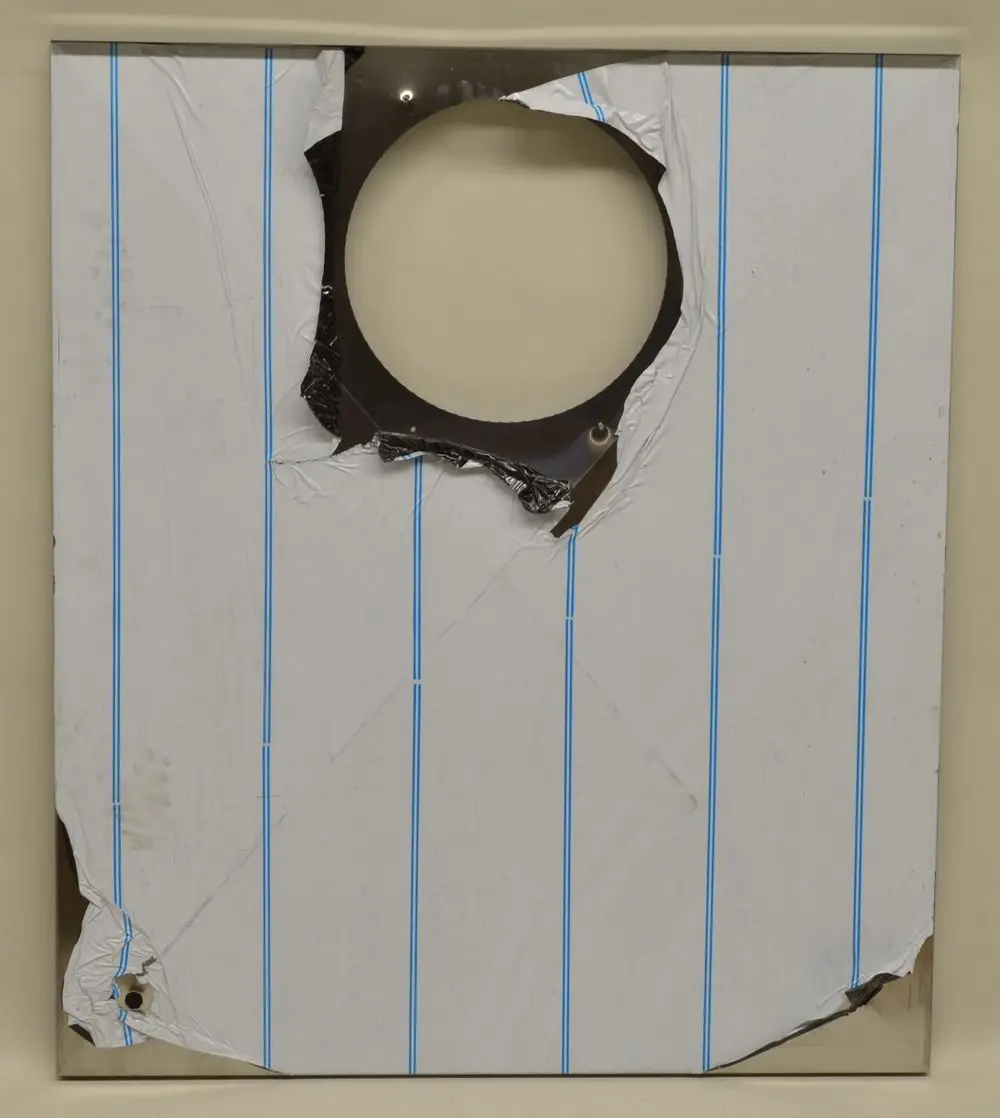 Deckblech von Remko, hintere Seite mit ausgerissener Stelle und Löchern, teilweise beschädigt, beschichtet mit weißem Papier und blauen Linien.