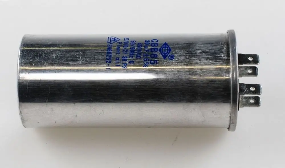Kondensator mit einer Metalloberfläche und mehreren Anschlussstiften, hergestellt von Remko. Der Kondensator ist typischerweise für den Einsatz in Kompressoren geeignet.
