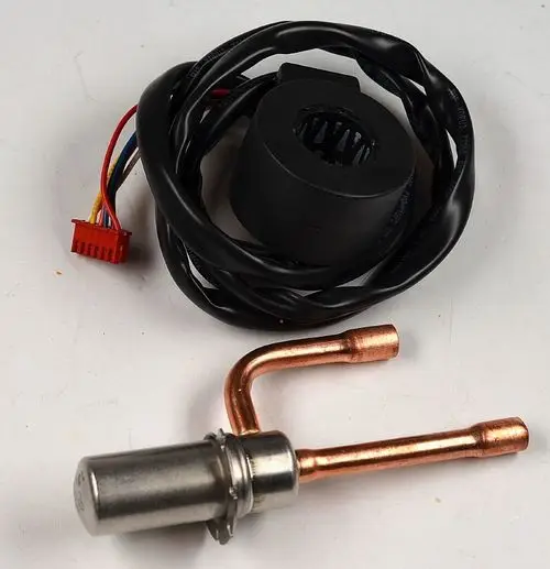 Elektronisches Ventil mit einem verchromten und einem kupferfarbenen Anschluss, umgeben von Kabeln. Das Produkt stammt von Remko.