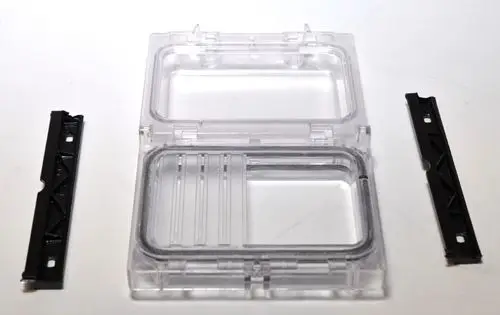 Durchsichtige Abdeckung mit separaten Bereichen und zwei schwarzen Halterungen. Das Produkt gehört zur Marke Remko und ist für die Befestigung gedacht.