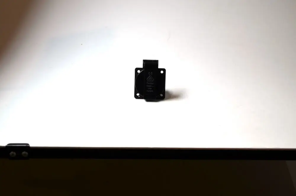 Stecker mit schwarzem Gehäuse und Schaltkontakt, platziert auf einer weißen Oberfläche. Produkt scheint von der Marke Remko zu sein.