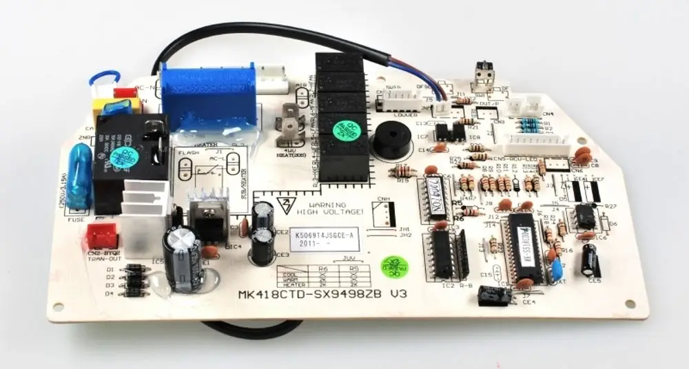 Steuerplatine von Remko mit mehreren elektronischen Bauteilen, Relais und Anschlüssen, auf einer hellen Leiterplatte angeordnet. Warnhinweis zu Hochspannung sichtbar.