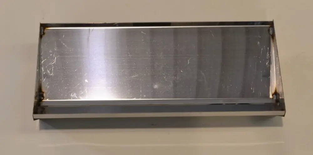 Einfache, rechteckige Metallplatte aus Edelstahl mit glatter Oberfläche und leicht lädierten Kanten, verwendet als Teil eines Remko Rauchgasumlenkers.