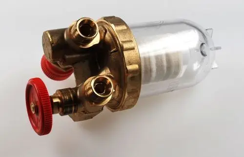 Ölfilter von Remko in kompakter Bauform mit zwei Anschlüssen. Klarsichtbehälter für die Sichtprüfung des Innenfilters und rote Verschlusskappen.