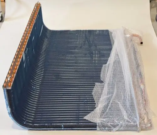Verflüssiger mit spiralförmigen Rohren und Kupferanschlüssen, verpackt in Folie. Produkt von Remko, auf einem hellen Hintergrund platziert.