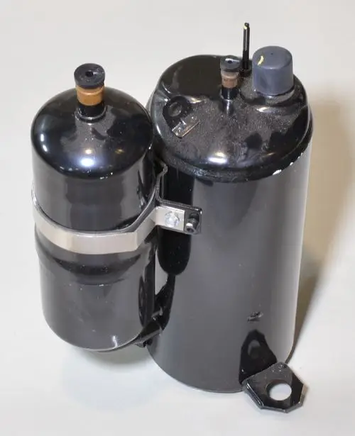 Schwarzer Kompressor mit zwei zylindrischen Teilen, montiert mit einer Metallklemme, Vorderseite hat Anschlussöffnungen. Produkt der Marke Remko.