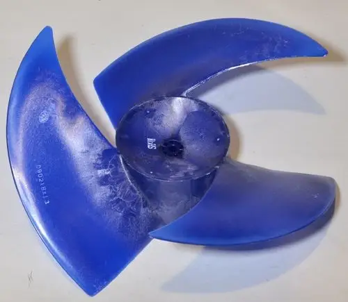 Blauer Ventilatorflügel von Remko, mit vier geschwungenen Klingen, auf einer weißen Oberfläche liegend, leicht verschmutzt.