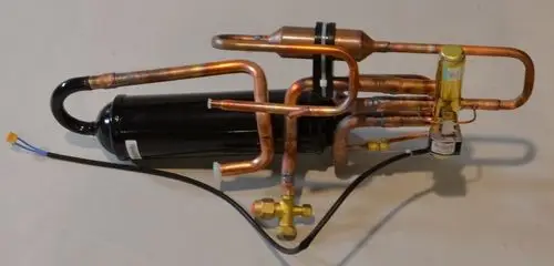 4-Wege-Umschaltventil von Remko mit mehreren Kupferrohren und einem schwarzen Kompressor. Das Gerät weist verschiedene Anschlussstellen auf und dient der Kühltechnik.