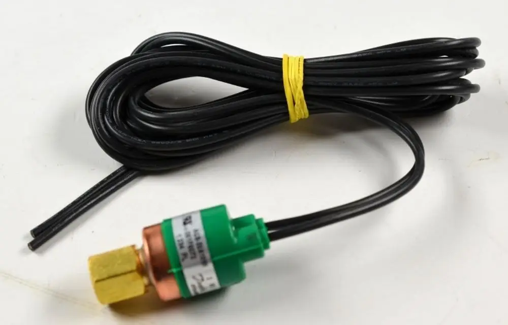 Niederdruckwächter von Remko mit einer grünen und braunen Anschlussmutter sowie zwei schwarzen Kabeln, die zusammengerollt und mit einem gelben Gummiband zusammengehalten sind.