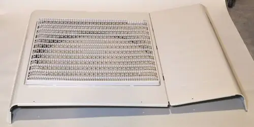 Weißes Frontpaneel mit Gitterstruktur, möglicherweise Teil eines Klimageräts, der Marke Remko, liegt auf einer neutralen Oberfläche.